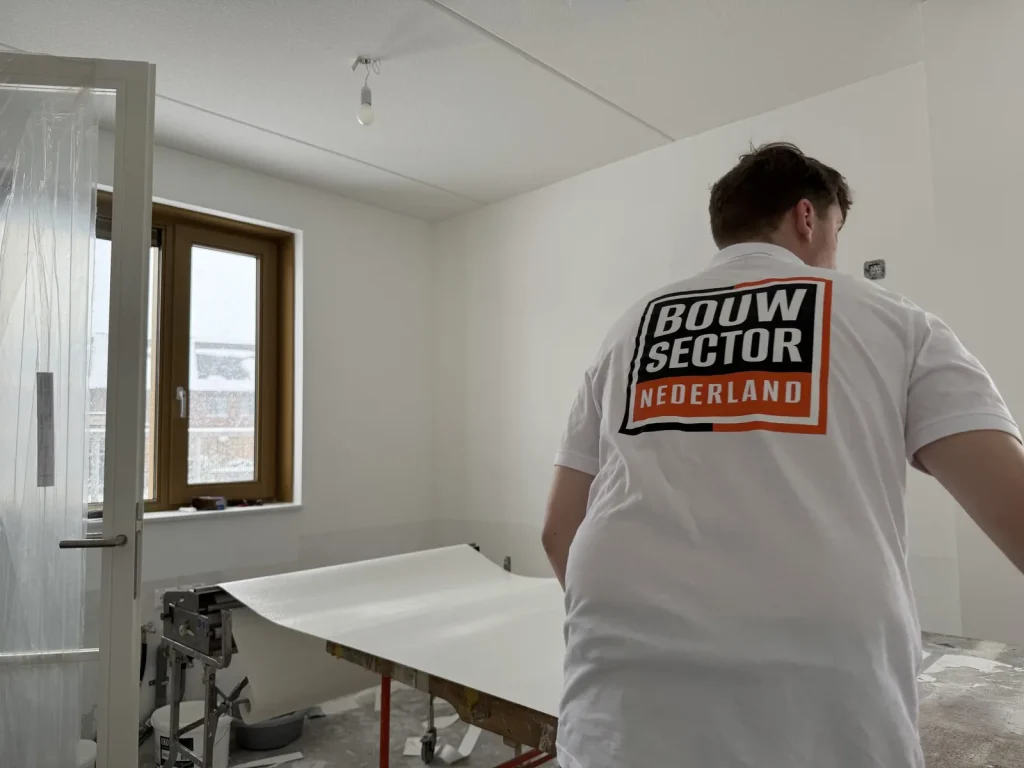 Behanger in een nieuwbouwkamer bij de plaktafel waar een baan vlies overheen ligt, met de deuropening in folie