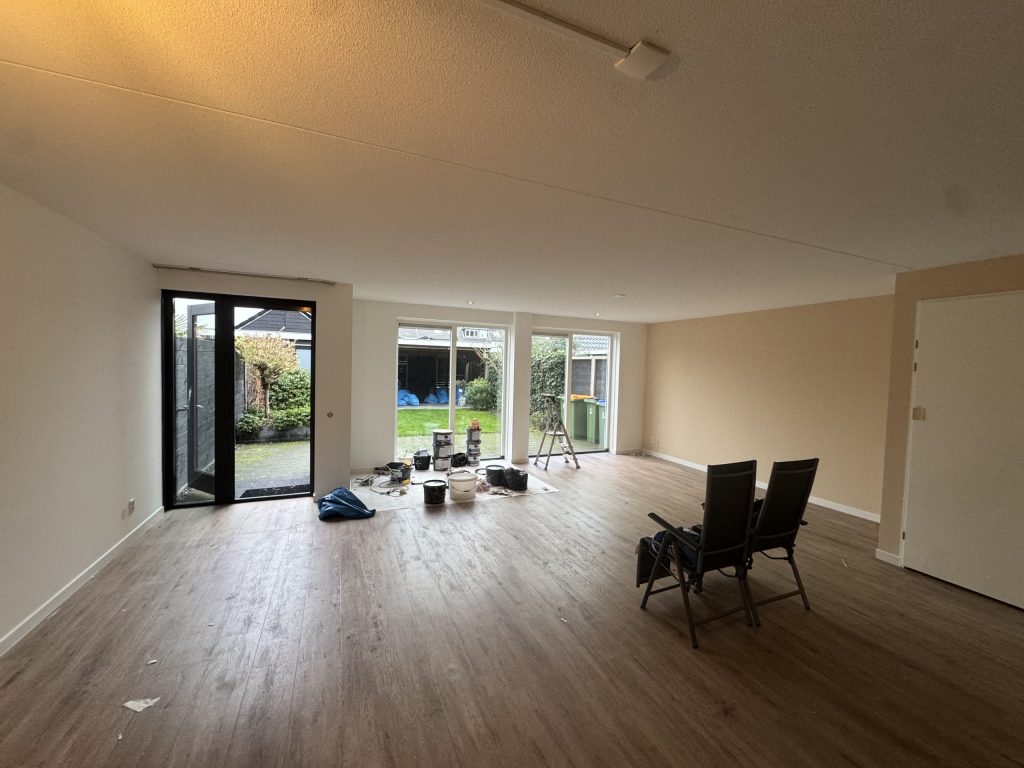 Ruime woonkamer met gesausde wanden, tuindeuren en verfemmers en een trapje op een afdekkleed